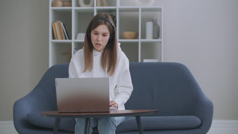 Young-woman-wears-headset-conference-calling-on-laptop-talks-with-online-teacher-studying-working-from-home.-Lady-student-e-learning-using-computer-webcam-chat-makes-notes.-Distance-education-concept